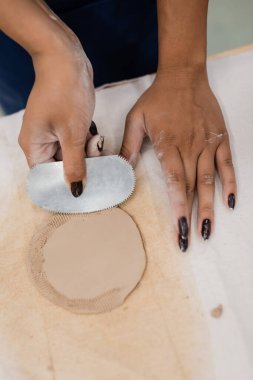 top view of african american woman with manicure holding steel scraper while shaping clay piece  clipart