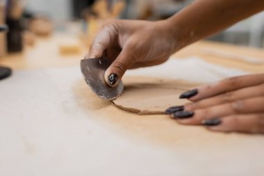 cropped view of african american woman with manicure holding stainless steel scraper while shaping clay piece  clipart