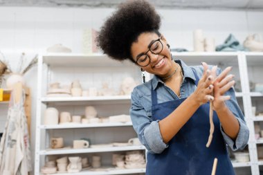 Cheerful african american craftswoman forming clay in pottery workshop  clipart