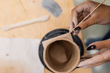 Top view of african american craftswoman making ceramic product with wooden stick in pottery studio  clipart