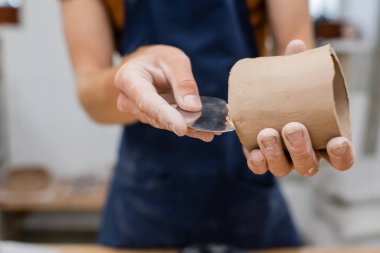 Cropped view of sculptor forming clay product with steel scraper in pottery workshop  clipart