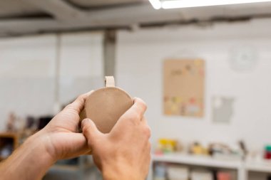 Cropped view of craftsman holding clay cup in blurred pottery workshop  clipart