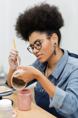 Çömlek atölyesinde seramik ürün üzerine genç Afrikalı Amerikalı esnaf resim yapıyor. 