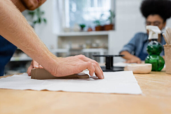 cropped view of man pressing clay piece with hand near african american woman 