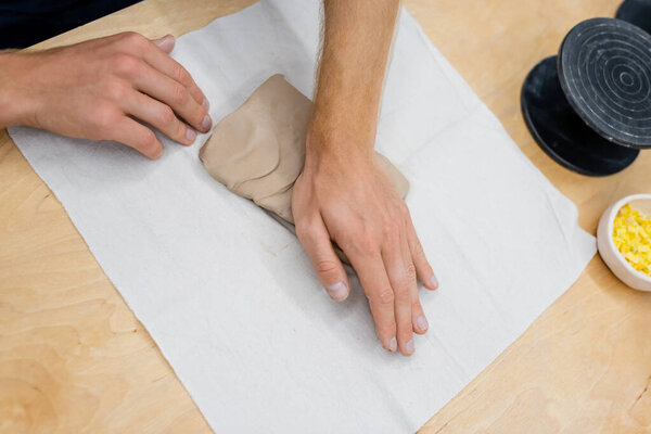 top view of cropped man pressing clay piece with hand during pottery class
