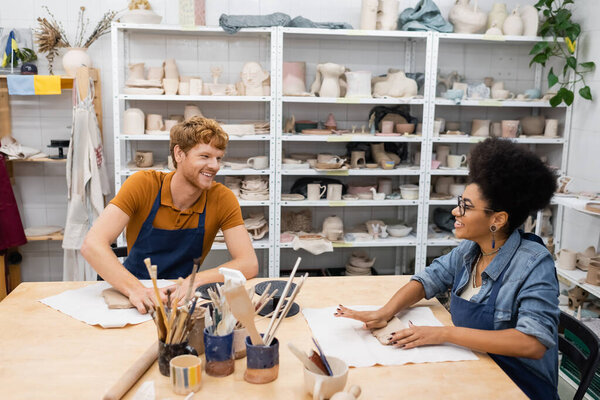 happy interracial couple smiling while shaping clay during pottery class 