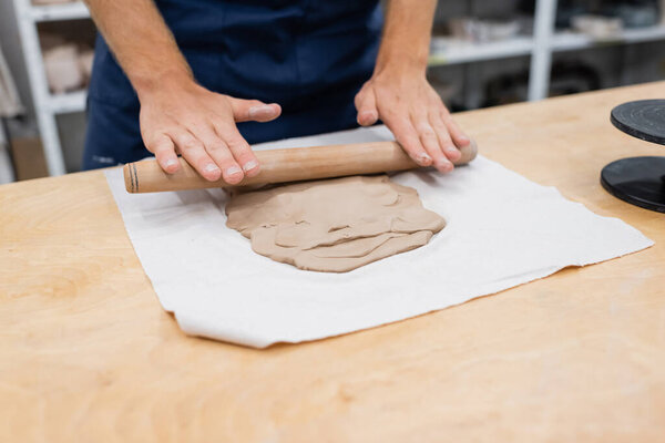 cropped view of man in apron shaping clay piece with rolling pin during pottery class 