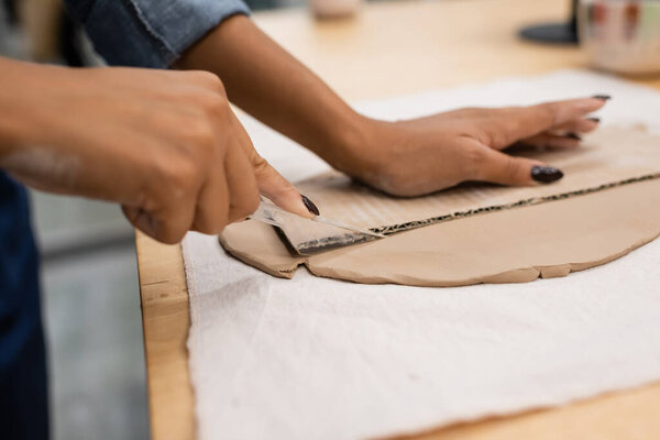 cropped view of african american woman cutting clay with knife near carton 