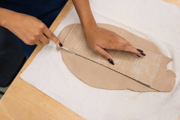 top view of african american woman cutting clay with knife near carton 