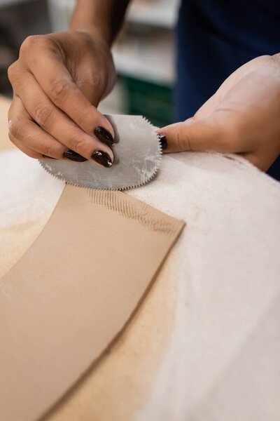 cropped view of african american woman holding steel scraper while shaping clay 
