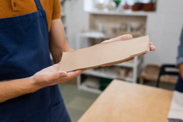 cropped view of man in apron holding rectangle shape clay piece in hands