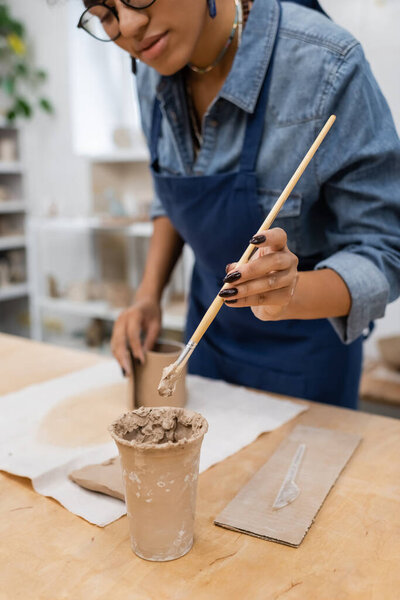 cropped view of african american woman in eyeglasses holding clay shaper 