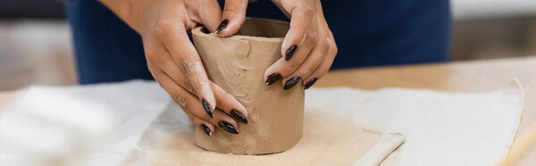 partial view african american woman with manicure shaping clay during pottery class, banner