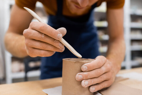 cropped view of concentrated man holding shaper while modeling clay cup in pottery workshop