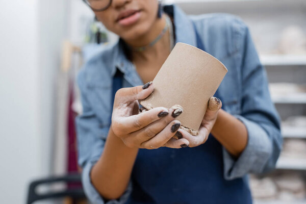 cropped view of african american woman molding clay cup in hands