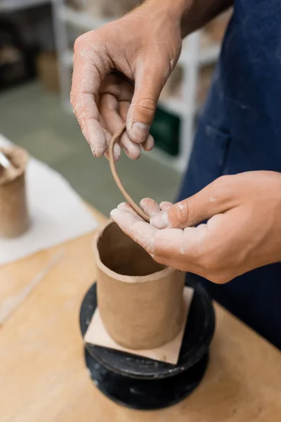 陶芸スタジオでぼやけた彫刻の近くに粘土を保持する男の作物ビュー — ストック写真
