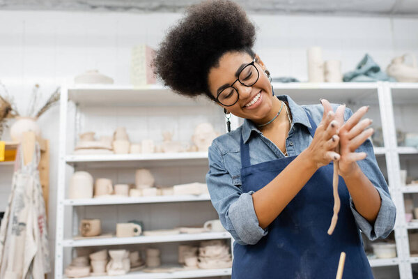 Cheerful african american craftswoman forming clay in pottery workshop 