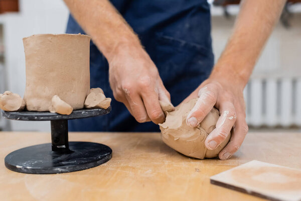 Cropped view of sculptor taking clay near cup in pottery workshop 