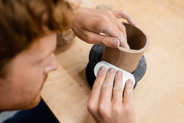 Blurred man holding tool while making ceramic sculpture in pottery studio 