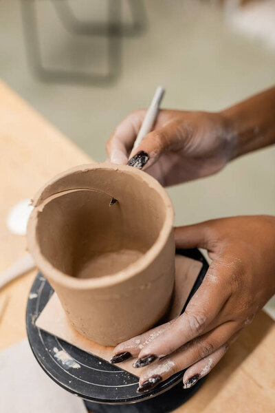 Cropped view of african american craftswoman cutting clay in pottery workshop 