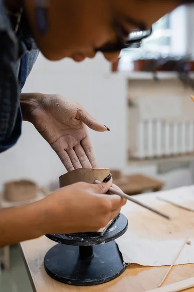 Blurred african american master making clay sculpture in pottery workshop