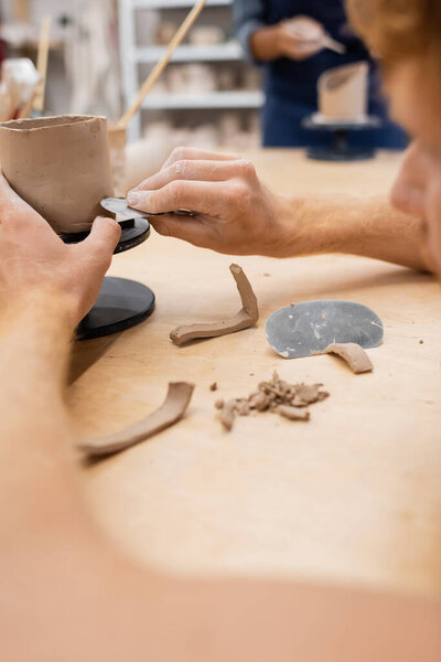 Cropped view of man making clay cup with tool in pottery workshop 