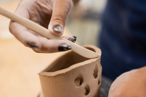 Close up view of african american craftswoman using tool while making clay product in workshop 
