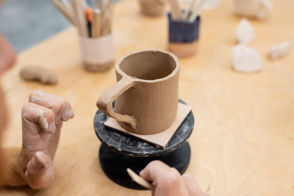 Cropped view of artisan making ceramic cup in pottery workshop 