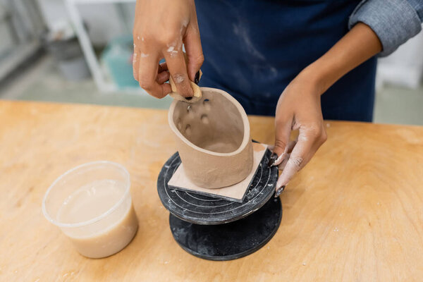 Cropped view of african american craftswoman forming clay sculpture with sponge in pottery workshop 
