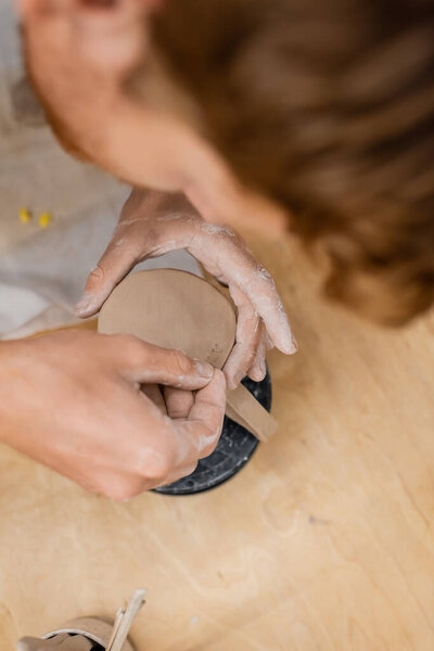 Overhead view of artisan creating signs on clay cup in pottery workshop 