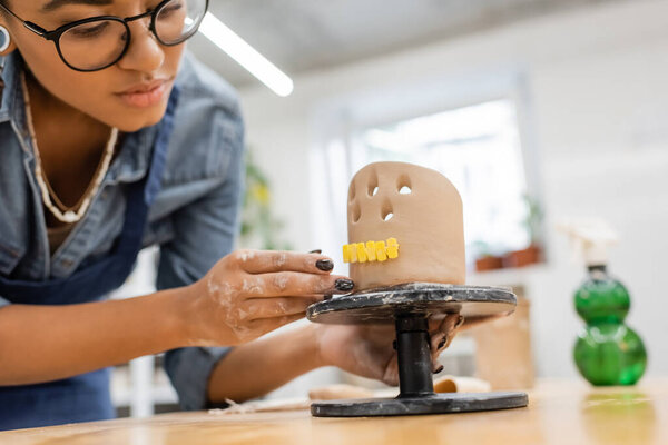 Young african american master in eyeglasses making clay sculpture in pottery workshop 