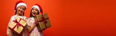 Noel Baba şapkalı neşeli ergen kızlar turuncu ve pankartta izole edilmiş Noel hediyeleri taşıyorlar.