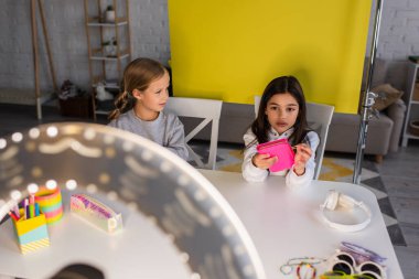 Video blogcusu kalem kutusunu arkadaşının yanında tutuyor ve ön planda bulanık halka ışığı