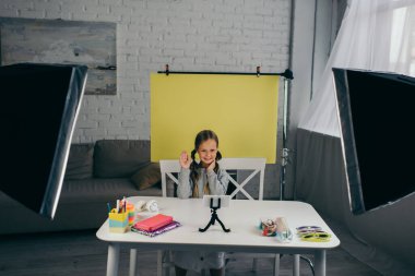 Ergen video blogcusu akıllı telefonun yanında el sallıyor ve masadaki farklı aksesuarlar 