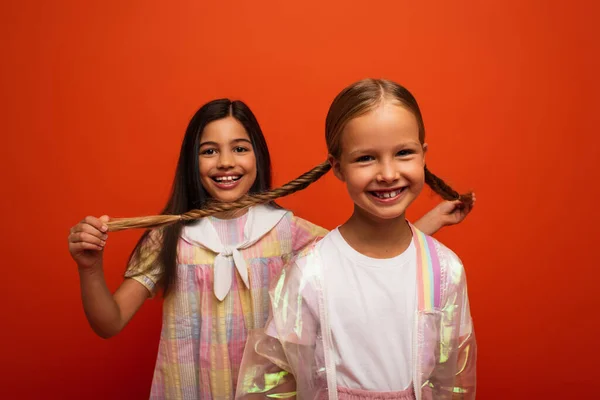 Smiling Girl Holding Pigtails Happy Friend Looking Camera Isolated Orange — Stock Photo, Image