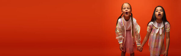 девочки-подростки держатся за руки и гримасируют с открытыми ртами перед камерой, изолированной на оранжевом, баннер