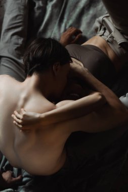 Üstsüz adamın sarılıp öptüğünü ve atölyede örtü giymiş gülümseyen Afrikalı Amerikalı kız arkadaşı.