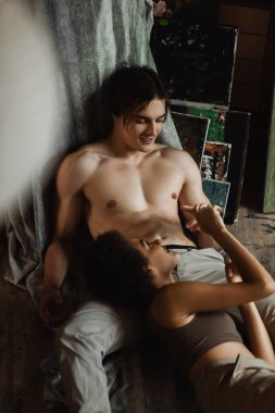 Sanat atölyesinde seksi üstsüz erkek arkadaşının elini tutan mutlu Afrikalı Amerikalı kadın.
