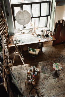 Sandalye ve sehpanın yanındaki pencere pervazında geniş pencereli ve sanat aletleriyle geniş bir atölye 