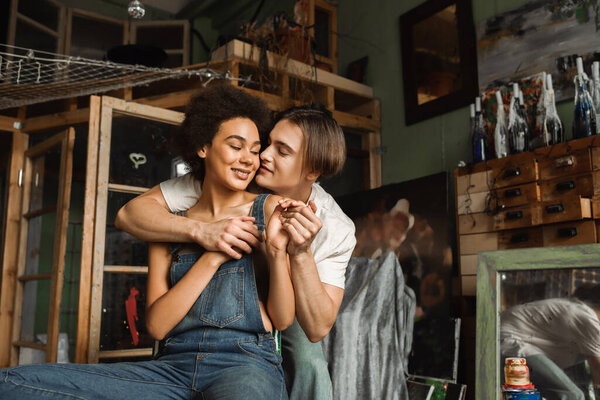 smiling african american woman in denim overalls holding hands with boyfriend in art studio