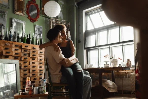 Young Multiethnic Artists Embracing Chair Workshop Large Window Vintage Furniture — Stock Photo, Image