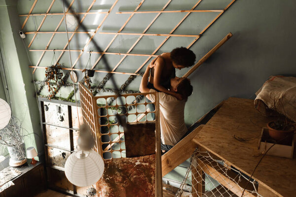 sexy interracial couple embracing on stairs near decorative grid in art workshop