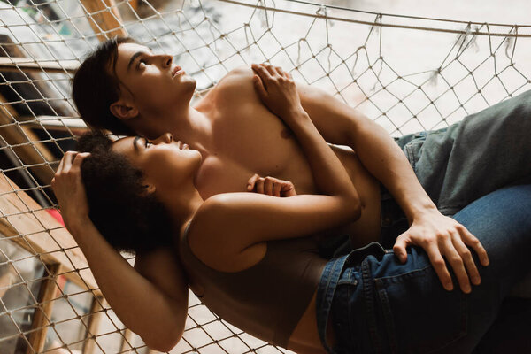 top view of young interracial couple embracing and looking away in mesh hammock