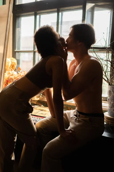 サイドビューの白人男性でパンツのキスセクシーアフリカ系アメリカ人女性近くのウィンドウでアートスタジオ — ストック写真