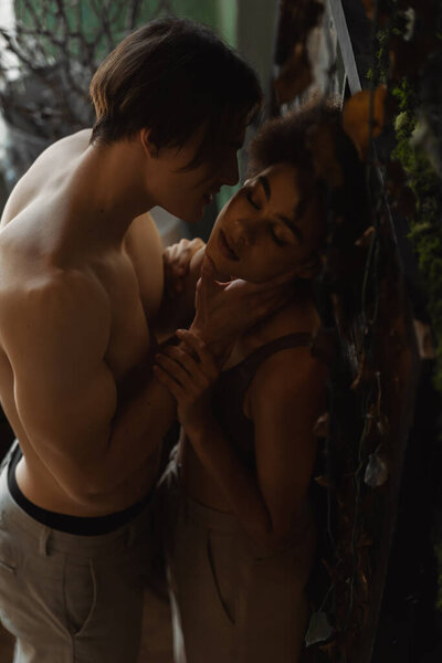 sexy man with muscular body touching face of african american woman with closed eyes in art studio