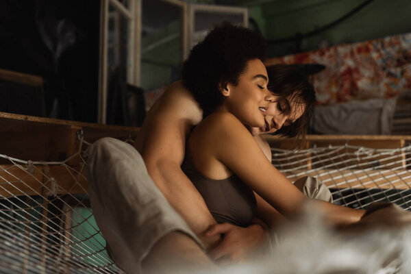 young man embracing sensual african american girlfriend while sitting in hammock