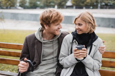 Şemsiyeli mutlu genç adam bankta otururken sarışın kız arkadaşına sarılıyor.