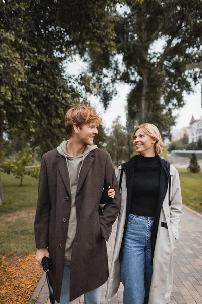 幸せな赤毛の男と陽気なブロンドの女性は秋の公園を歩いている間にお互いを見て — ストック写真