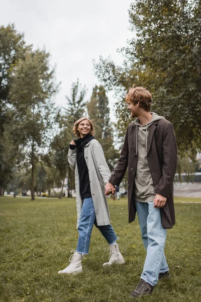 全身上下都是身穿外套的年轻人 在秋天的公园散步时 与快乐的女朋友牵着手 — 图库照片