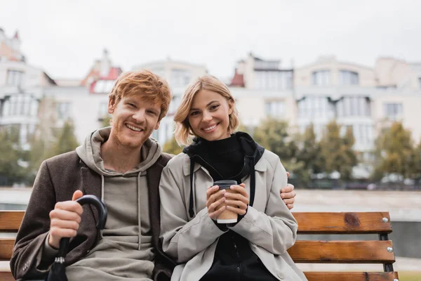 Gelukkig Jongeman Met Paraplu Knuffelen Vriendin Holding Papier Beker Terwijl — Stockfoto